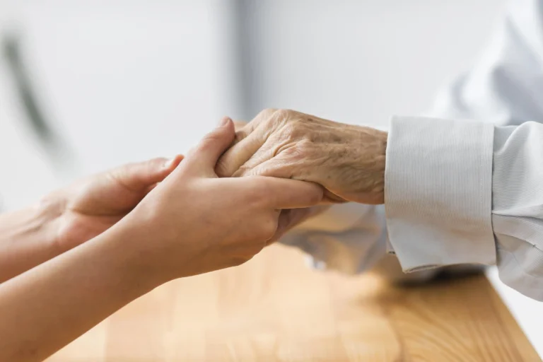 A nurse gently holding a senior man's hands, offering comfort and support.
